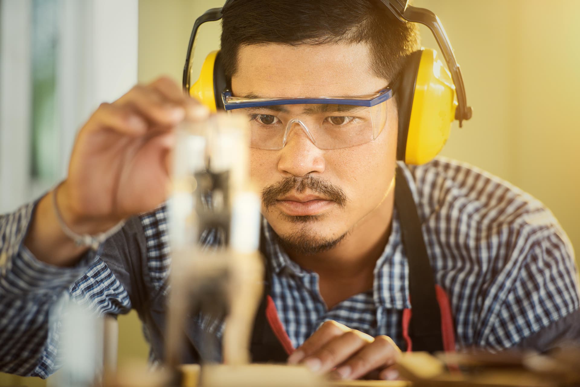 Technicien concentré avec casque antibruit et lunettes de sécurité, illustrant les contrôles qualité rigoureux.